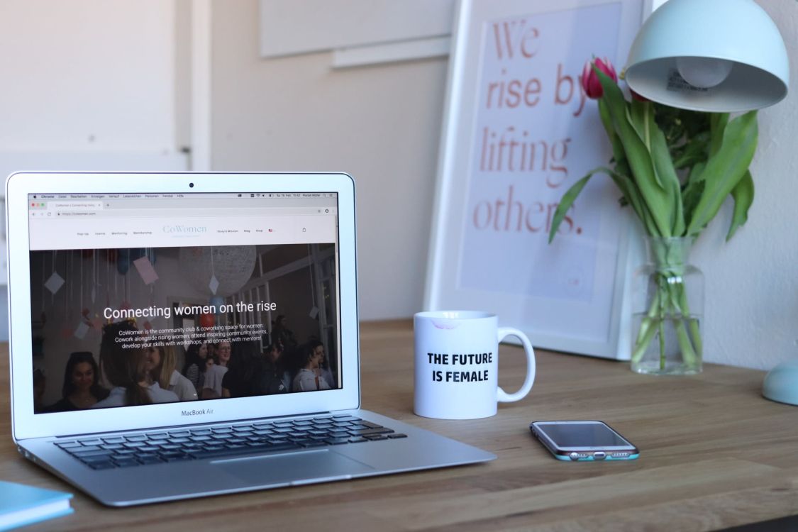 Computer, Kaffeetasse und Handy auf einem Schreibtisch. Auf dem Bildschirm steht: "Connecting women on the rise". Auf der Tasse steht: "THE FUTURE IS FEMALE"