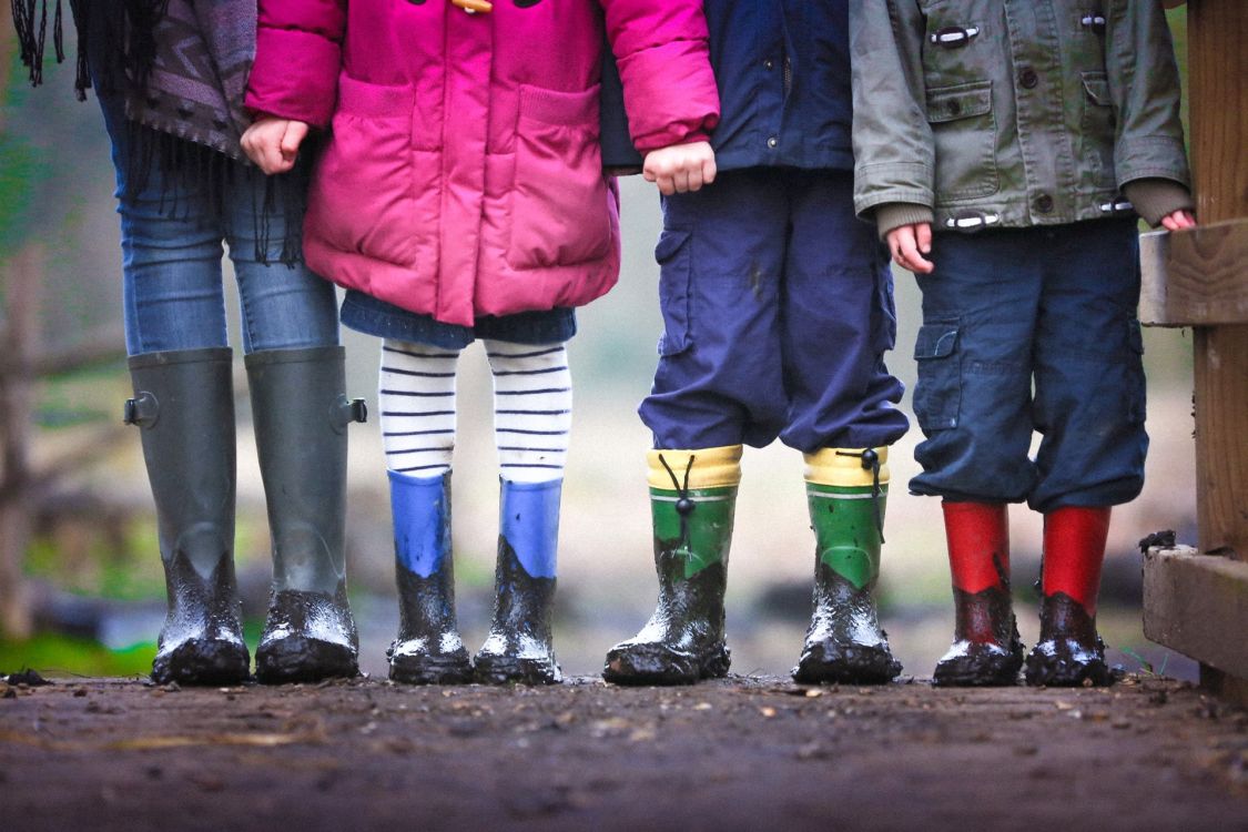 Eine erwachsene Person und drei Kinder mit schlammbeschmierten Gummistiefeln