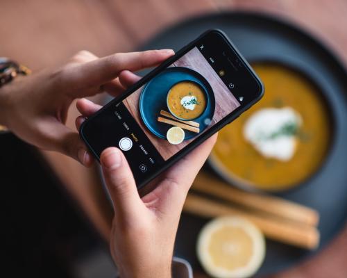 Jemand macht mit dem Handy ein Foto von einer orange-farbigen Suppe